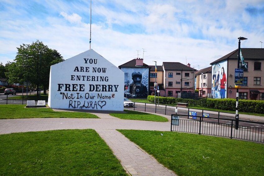 A large white sign with graffiti, a paved walkway, and buildings in the background. 1