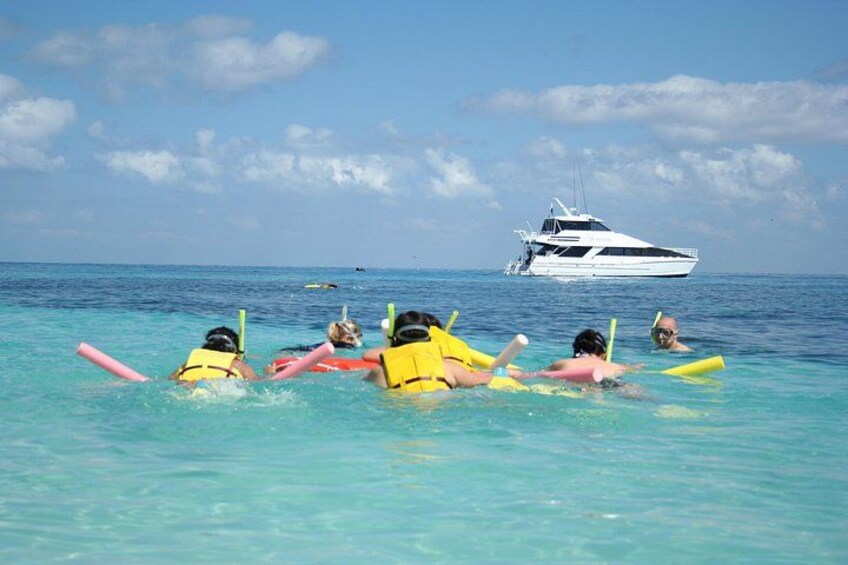 People snorkeling in clear blue water with a yacht in the background. 2