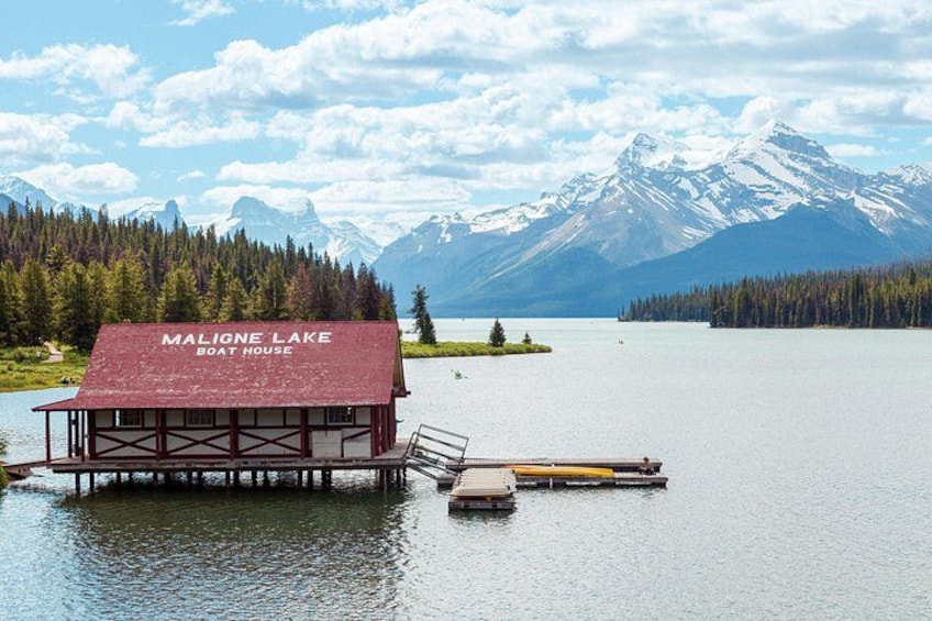 Ein Bootsanleger namens Maligne Lake Boat House mit einer Anlegestelle, die sich in einen See erstreckt, umgeben von Bergen und Wald. 3