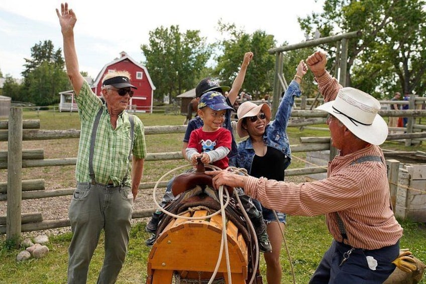 Un groupe de personnes interagissant avec une calèche tirée par des chevaux, dans un cadre extérieur agrémenté d’une clôture en bois et, au fond, d’une grange rouge. 2