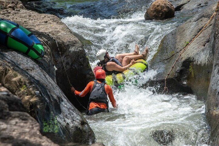 Una persona en un bote salvavidas amarillo navegando un río con rápidos, rodeada de rocas. 1