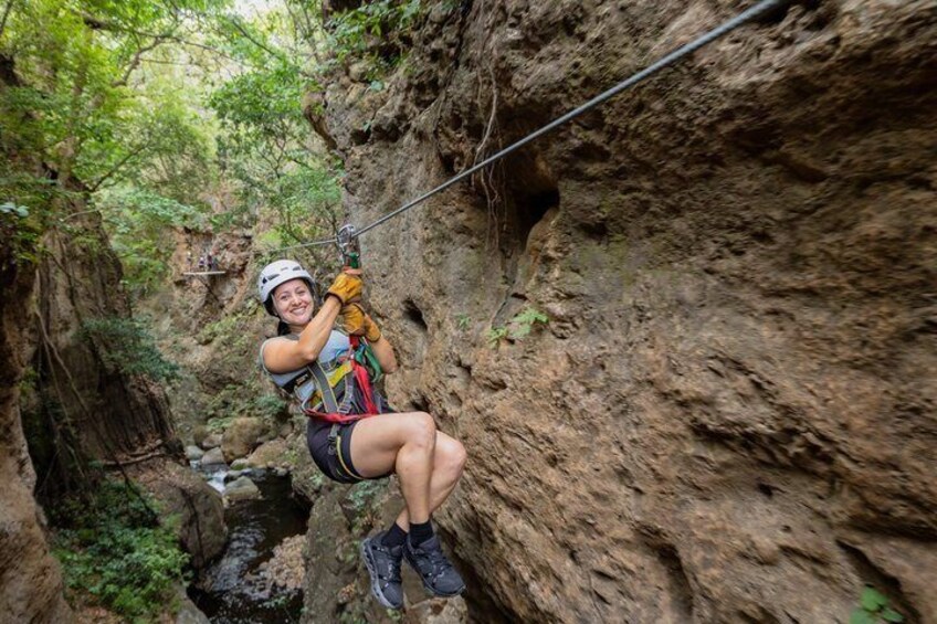A person zip-lining through a rocky canyon with greenery around. 1
