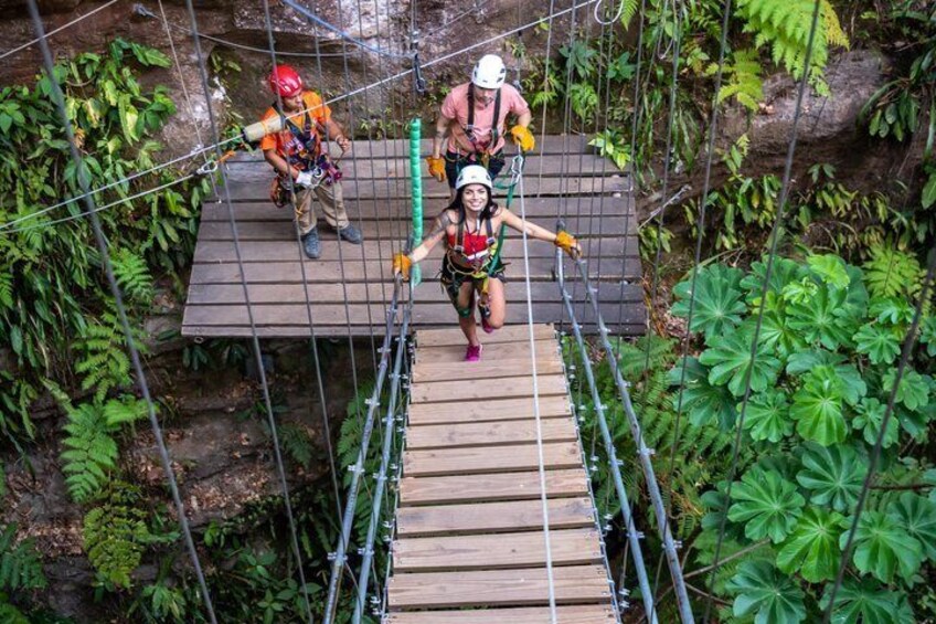 People on a suspended wooden bridge in a forested area. 2