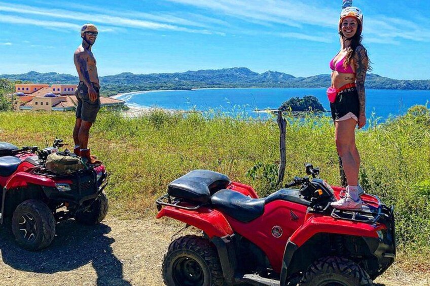 Two people on ATVs, a coastal landscape with mountains, and a clear blue sky. 2
