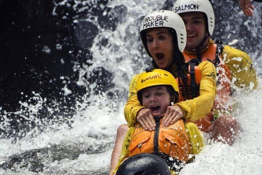 A person in a yellow jacket and helmet, another in a white helmet, and a child in a yellow helmet, all wearing life jackets, being swept by water. 5