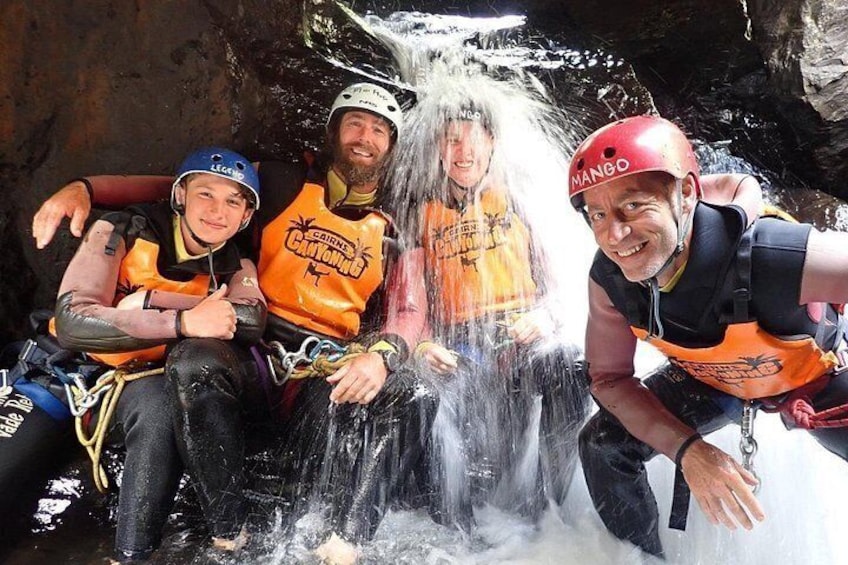 Four people sitting by a waterfall, wearing helmets and life jackets. 4