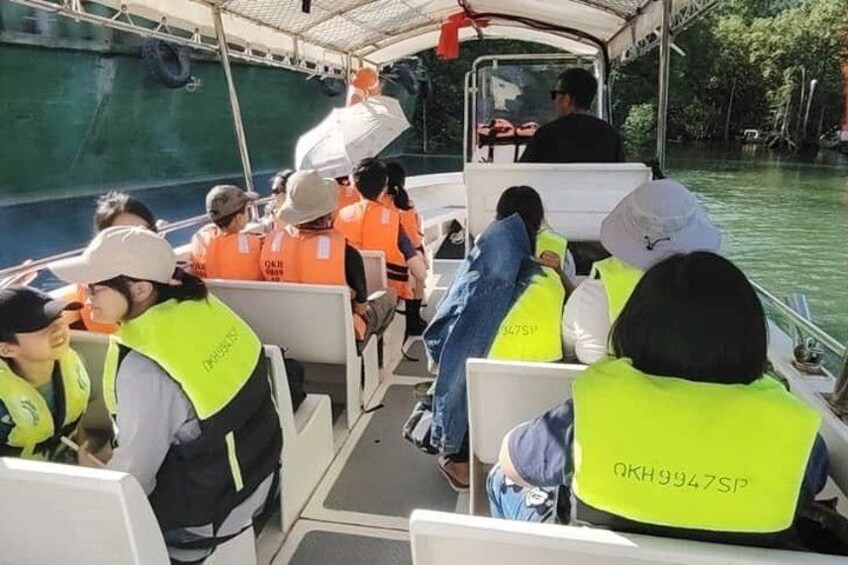 People on a boat wearing life jackets, with a green water body and trees in the background. 5