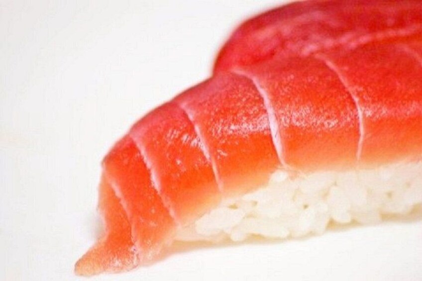 Une portion de sushi recouverte d'une garniture rouge, vraisemblablement du saumon, posée sur un lit de riz blanc. 2