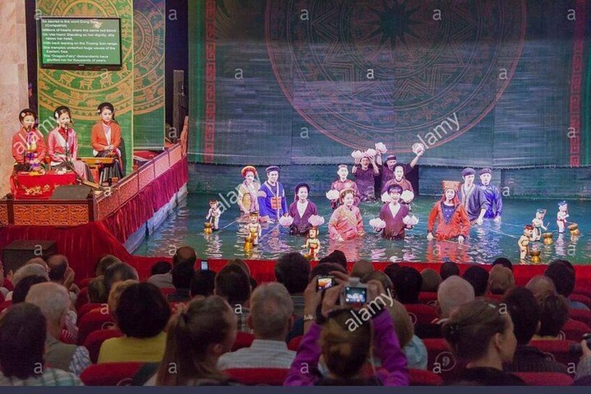Una rappresentazione teatrale con attori in costumi tradizionali, un vasto pubblico e uno sfondo decorato con motivi circolari. 2
