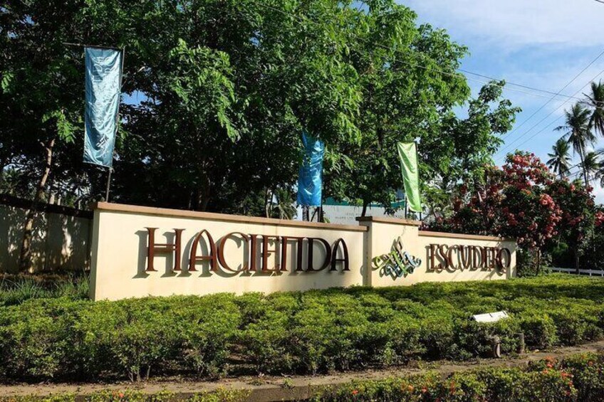 A sign with 'Hacienda Escudero' written on it, surrounded by greenery and trees. 5