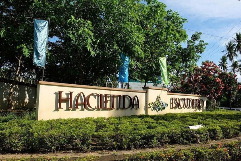 A sign with 'Hacienda Escudero' written on it, surrounded by greenery and trees. 2