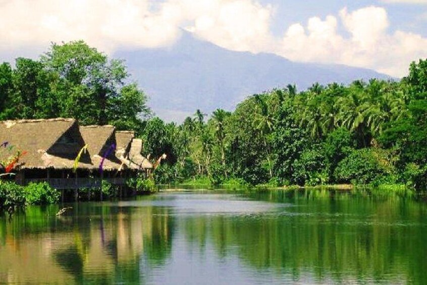 A river with thatched-roof huts, dense greenery, and a mountain in the background. 4