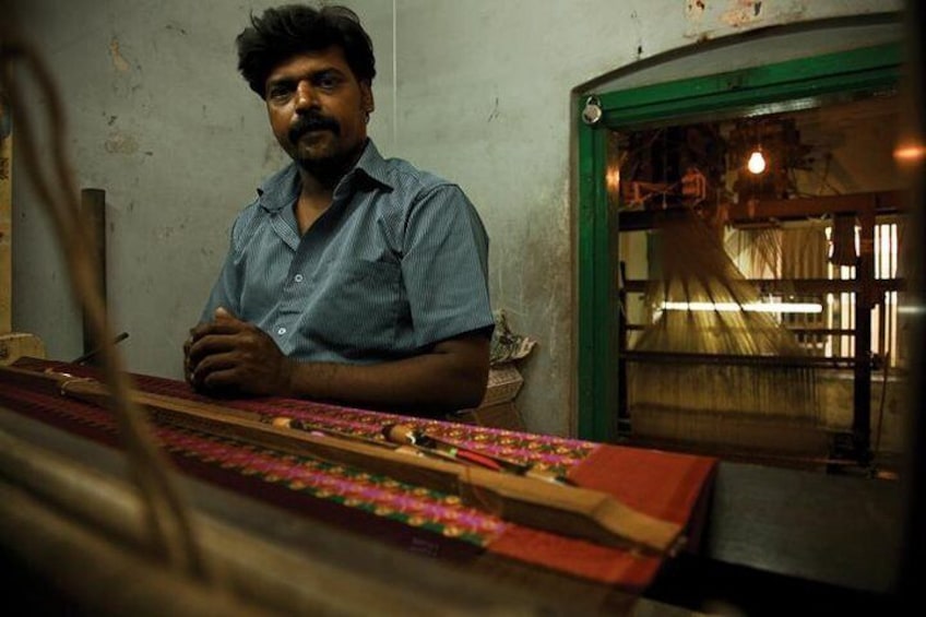 A person sitting at a loom with a red and black patterned fabric. 4