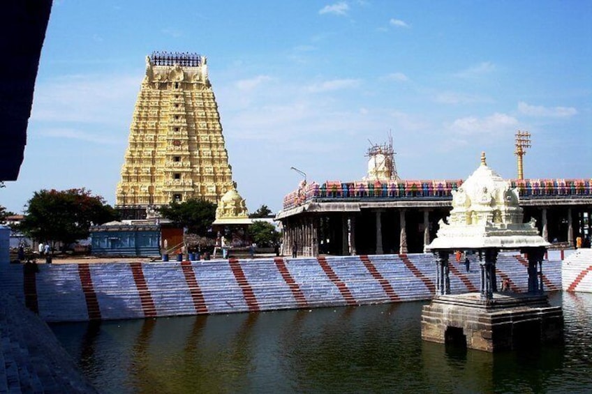 A temple with a large gopuram, a water body, and a white shrine. 5