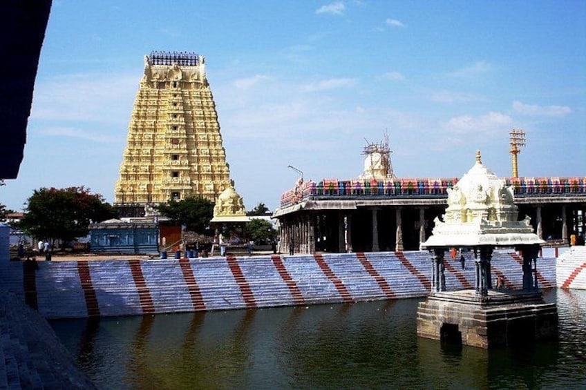 A temple with a large gopuram, a water body, and a white shrine. 5