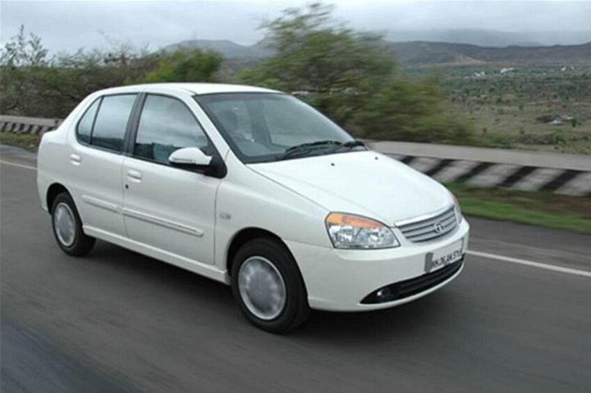 A white car driving on a road with a hilly landscape in the background. 2