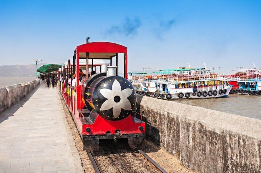 Un tren rojo con un diseño floral en la parte delantera, circulando sobre rieles junto a un cuerpo de agua con barcos. 1