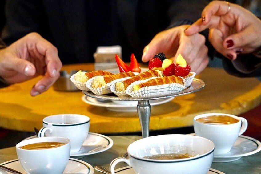 Une personne présente un dessert sur un présentoir, décoré de fraises et surmonté d’un fruit rouge. Il y a des tasses de café sur la table. 2
