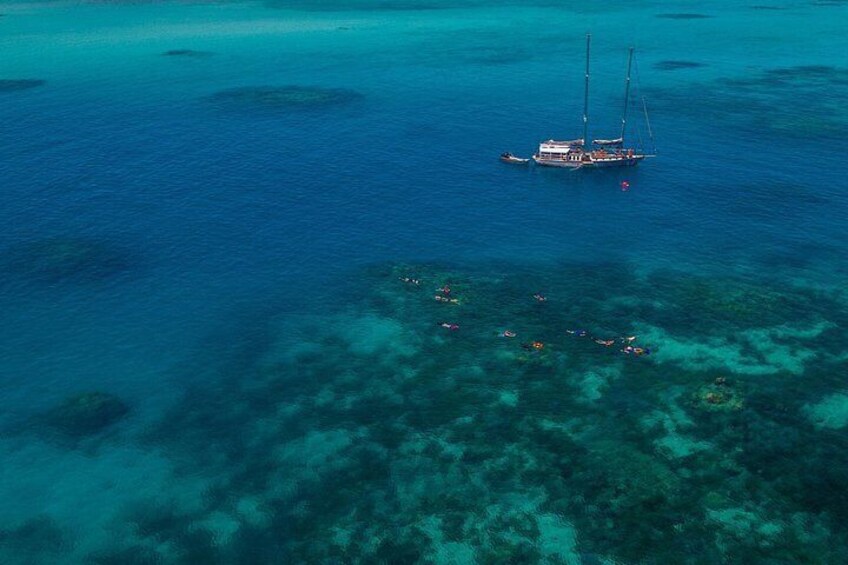 A sailboat on turquoise waters with clear shallow areas and a group of people swimming. 4