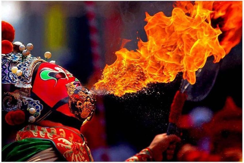 A performer with a mask and traditional attire, surrounded by flames. 1