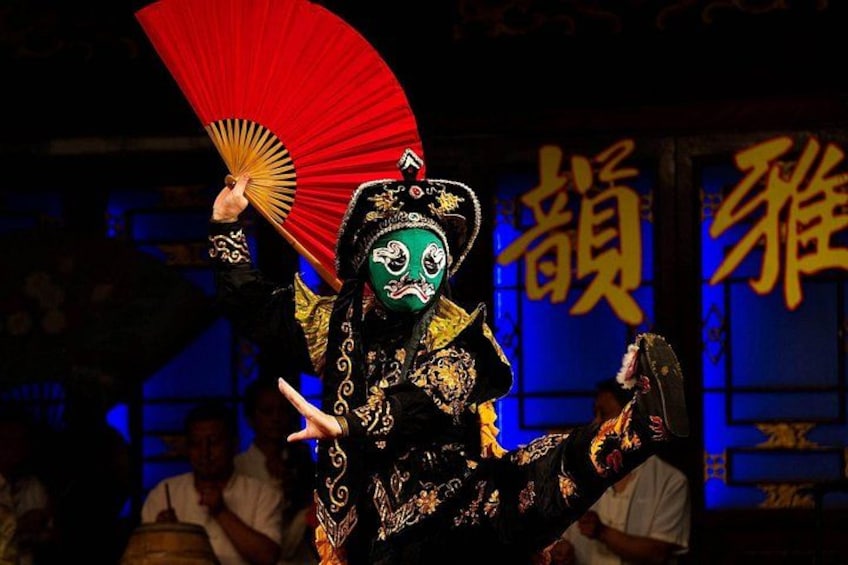 A performer in traditional costume with a red fan, performing on a stage with blue lighting and Chinese characters in the background. 5