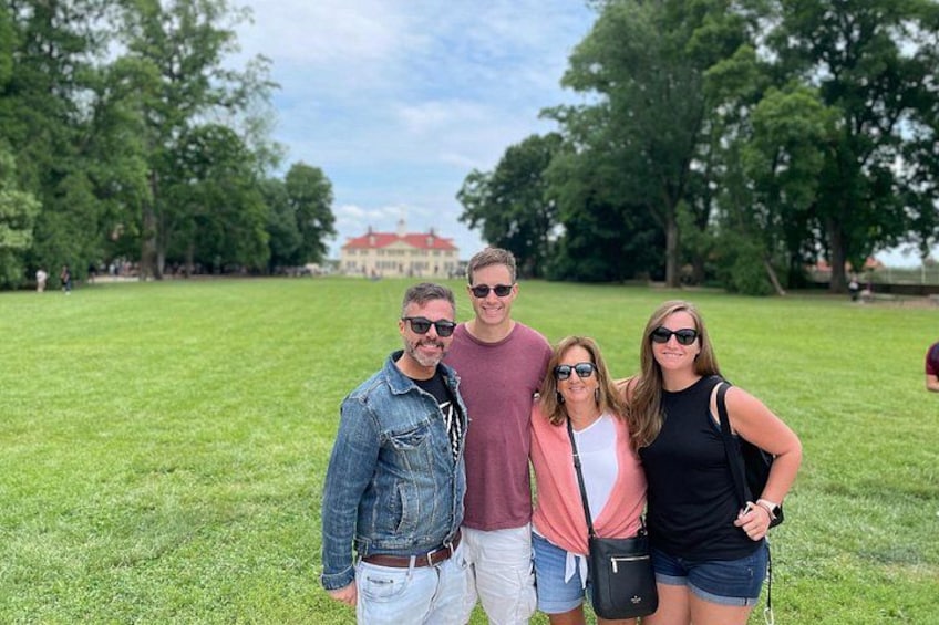 A group of people standing on a grassy field with trees and a building in the background. 1
