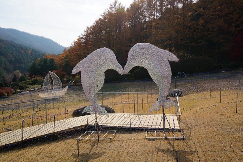 A sculpture of two dolphins leaping, surrounded by a fence and a wooden platform. 5