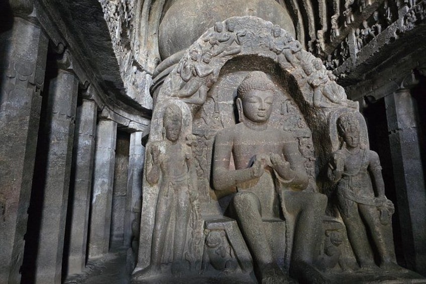 A stone carving of a seated figure with two attendants, surrounded by intricate carvings. 1
