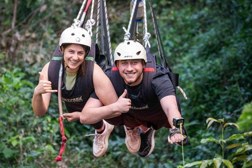 Two people suspended in a harness, wearing helmets, and smiling. 3