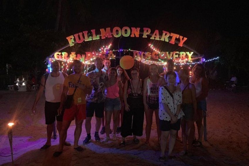 En grupp människor som står under en skylt med texten ”FULLMOON PARTY” en natt. 5