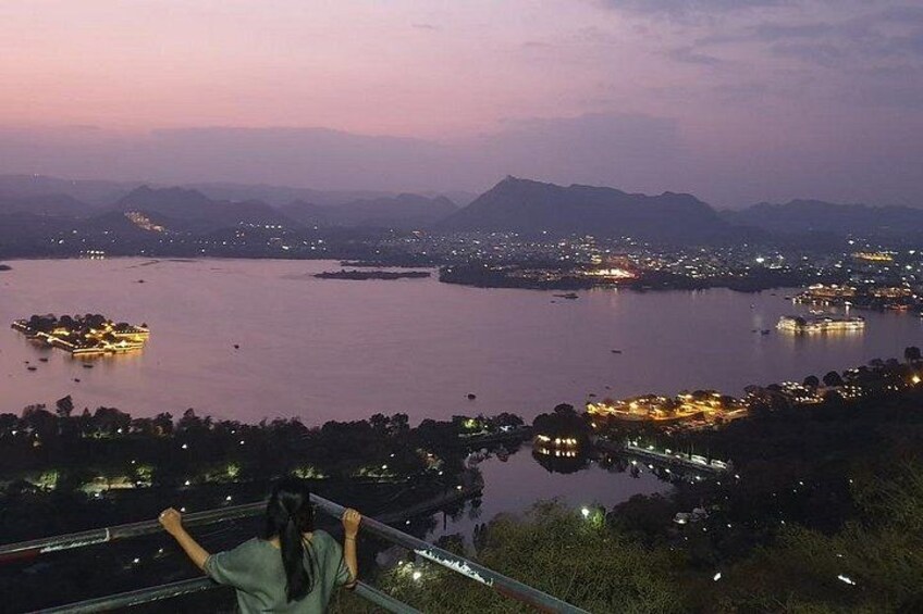 A panoramic view of a city at dusk with illuminated buildings and a large body of water. 2