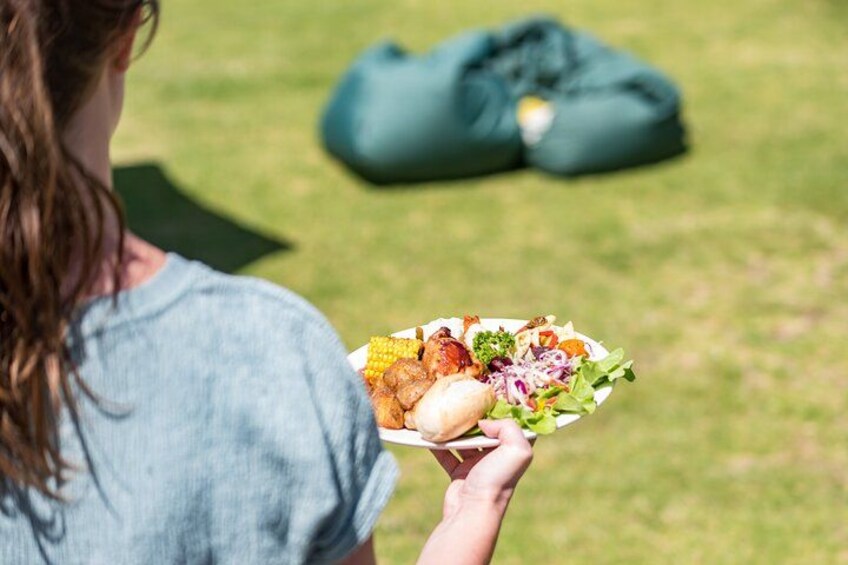 Una persona sosteniendo un plato con comida y una bolsa verde sobre el césped. 5