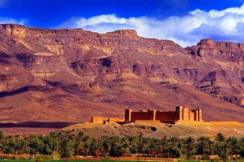 A desert landscape with a large sandstone structure, palm trees, and a mountain range. 2