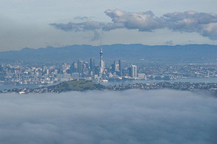 A city skyline with a prominent tower, surrounded by clouds and mountains in the background. 3