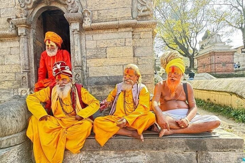 Tres personas vestidas con atuendos tradicionales sentadas en los escalones frente a una construcción de piedra. 1