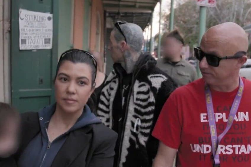 A street scene with people walking, a sign on a door, and a person wearing a red shirt. 1