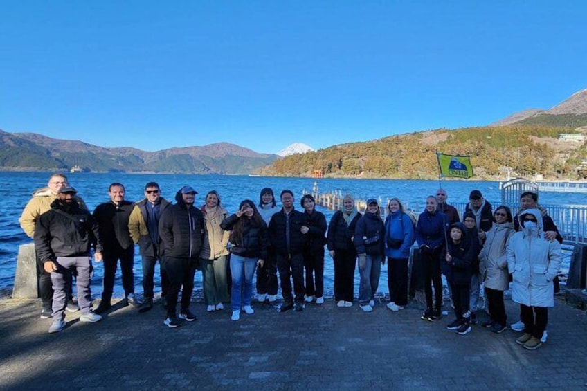 A group of people standing on a dock by a lake with mountains in the background. 4