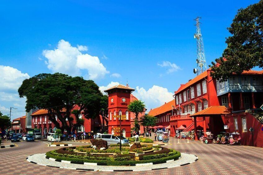 A red-bricked building with a clock tower, surrounded by a circular garden and a clear blue sky. 1