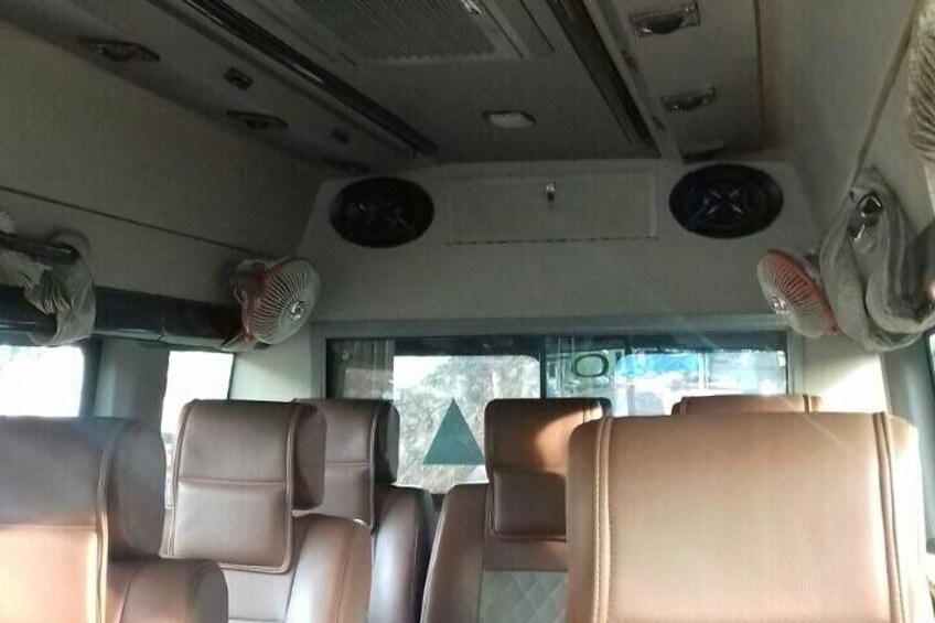 The interior of a bus with brown leather seats and ceiling fans. 2
