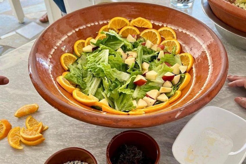 Una grande ciotola in terracotta piena di un'insalata con lattuga, mele e spicchi d'arancia. 3
