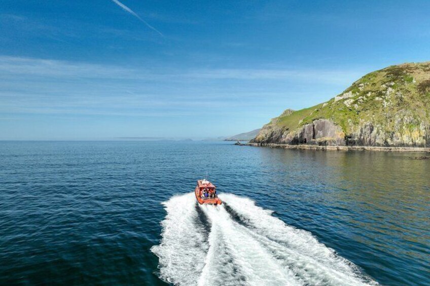 Un motoscafo rosso che scivola su un mare calmo, con una costa rocciosa sullo sfondo. 1