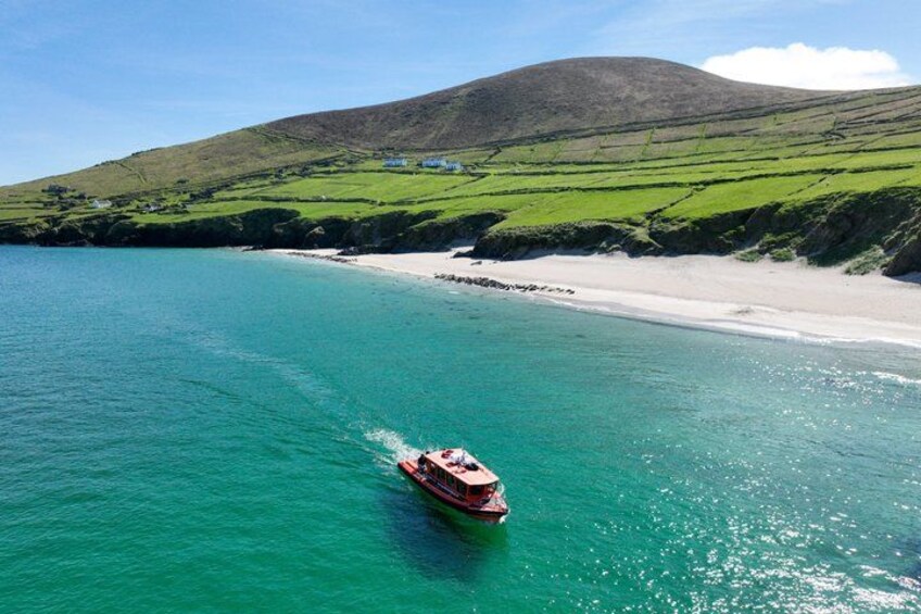 A boat on turquoise water, a sandy beach, and green hills in the background. 1
