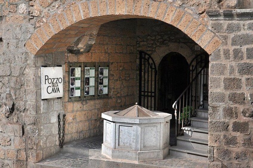 An arched stone structure with a sign reading 'Pozzo della Cava' and a stone fountain. 3