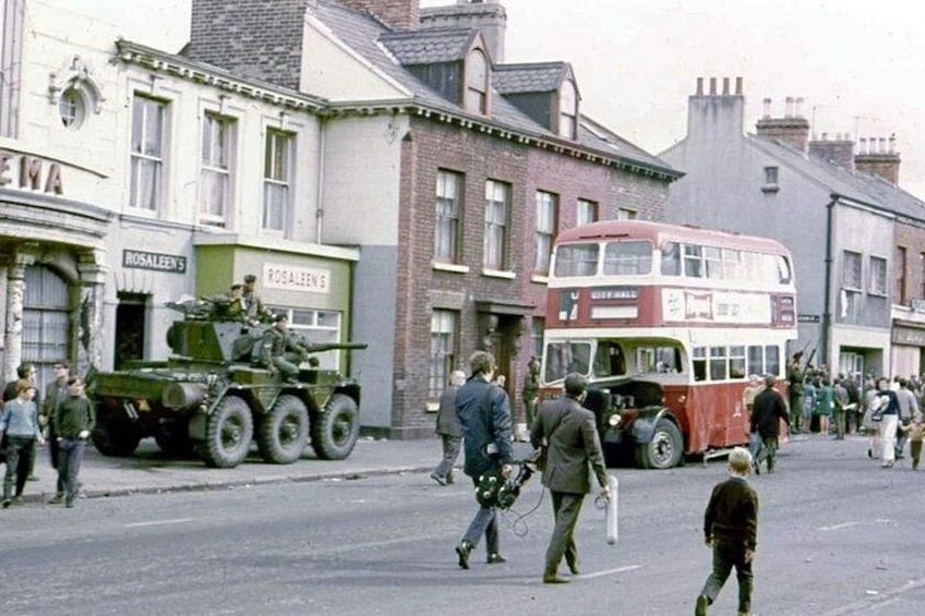 A double-decker bus, a military vehicle, and pedestrians on a street. 1