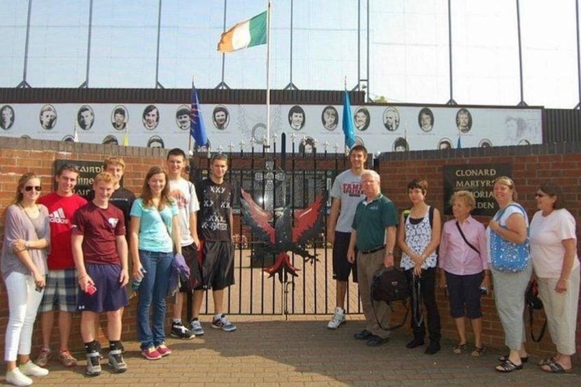 A group of people standing in front of a memorial wall with portraits and a flag. 2