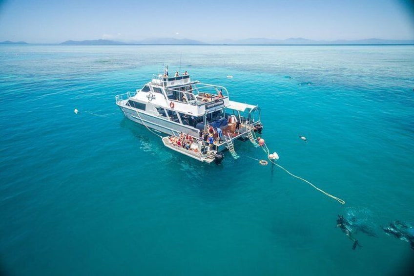 A boat anchored in clear turquoise waters with a few people on board. 2