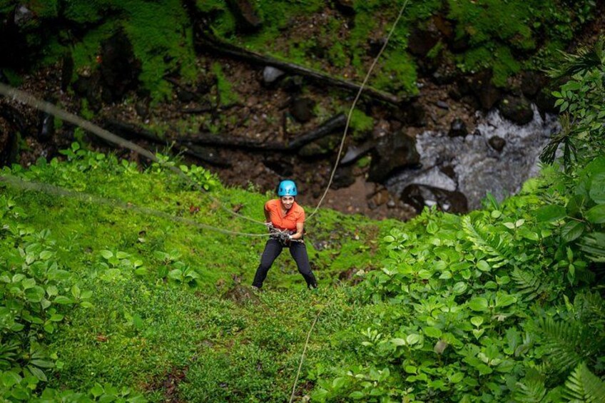 A person in an orange shirt and blue helmet engaged in zip-lining through a lush green forest. 3