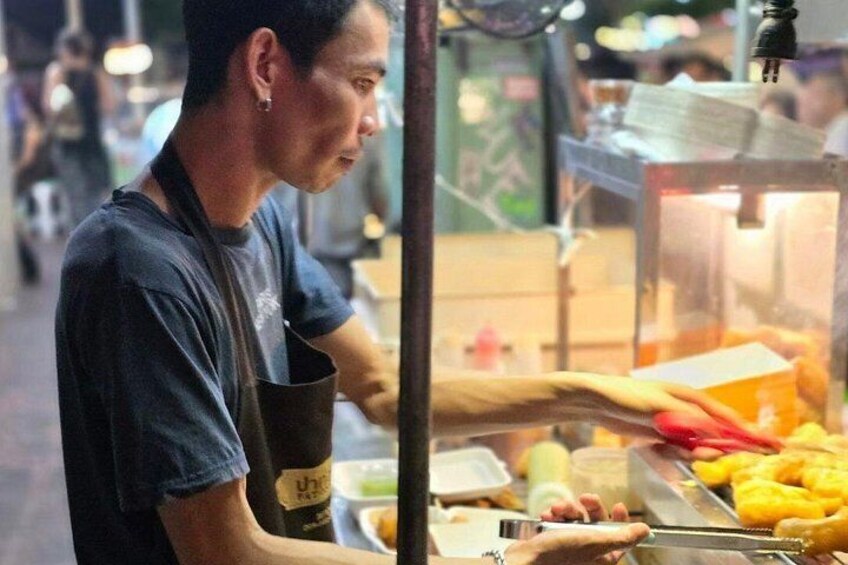 A person preparing food at a stall with various ingredients and utensils visible. 4
