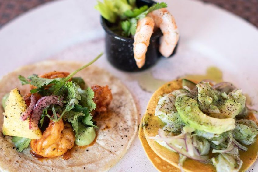 Two tacos with shrimp and avocado, and a small bowl of ceviche in the background. 3