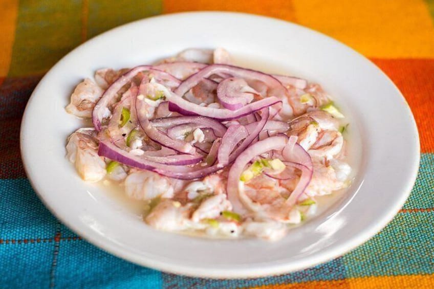 A white plate with a seafood dish, including shrimp and red onion slices, on a colorful tablecloth. 1
